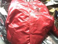 Red satin Chicago Bulls Mitchell & Ness jacket laid out showing front with button closure and embroidered small logo.