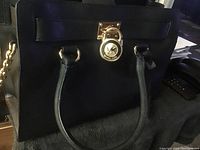 Front view of black Michael Kors purse with gold MK logo lock charm attached to the front flap.