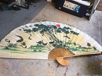 Full view of the large old Chinese fan opened showing crane, trees, and red sun artwork.