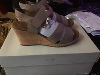 Side view photo of beige Rockport ladies wedge sandal on white box showing cork wedge heel and Velcro ankle strap.