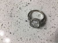 Silver halo ring with cushion-cut clear center stone and small clear stones around the halo seen from top.