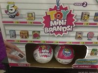 Front view of the two Toy Mini Brands Series 2 collectible balls displayed inside packaging with visible logos and colorful brand graphics.