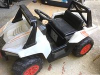 White U.T.V. 500 kids electric ride-on vehicle with large black tires and orange rims, black seat and steering wheel, shown from front-left angle on concrete floor.