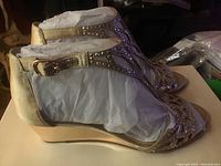 Side view of one shoe showing ankle strap, wedge heel, and studded design.