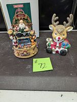 Front view of two musical boxes, Craftsman Santa Workshop on left with Santa and elves, reindeer with gifts on right