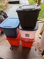 Five plastic storage bins stacked: two orange bins on the bottom, the white or clear bin above them, the blue bin next, and the brown bin on top, all with lids.