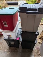 Stack of five plastic storage bins in various colors including black, red, white, and beige with lids visible.