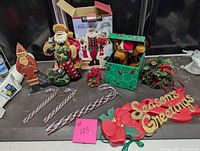 Photo showing the full lot of Christmas decor items on a table including the fabric Santa, wood Santa, Scooby Doo jack in the box, seasonal greenery, ornaments, and 'Seasons Greetings' hanger.