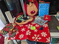 Full view of items including Christmas-themed red floor mat with snowflakes, reindeer toilet seat cover, blue snowflake tissue box cover, small Christmas towel, Christmas oven mitts and pot holders, and Christmas table runner.