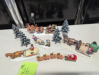 Overview of 4 snow-covered pine trees and 5 Christmas-themed sleigh figurines including horses and Santa figures.