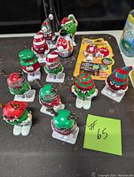 Twelve M&M's Christmas character figurines arranged on a dark surface, showing various characters in holiday costumes and hats.
