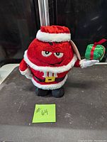 Front view of 12 inch red M&M plush dressed in Santa outfit holding wrapped present