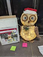 Full view of light-up owl sculpture wearing a red Santa hat, alongside its original packaging box.