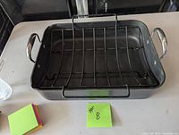 Pampered Chef rectangular roasting pan with metal handles and a black metal roasting rack inside.