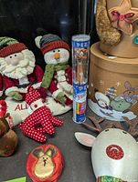 Photo showing Santa Claus and snowman plush figurines, red polka dot cloth reindeer, reindeer PEZ dispenser, and decorative boxes in background.