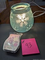 Lit Scentsy warmer showing textured blue glass with white snowflakes and included scent pack in front