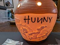 Close-up of the lit honey pot warmer showing 'HUNNY' and Winnie the Pooh characters embossed on the warm lighted ceramic design.