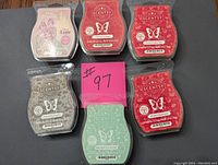 Photo of six Scentsy wax bars laid out on flat surface showing variety of scents and colors. Pink note with #97 placed in center.