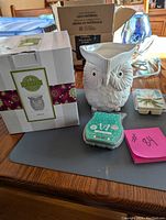 White ceramic owl-shaped Scentsy wax warmer burner on a table beside its box and two wax melt packages.