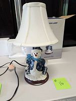 Front view of snowman lamp with white fabric shade showing details on snowman base and lamp shape.