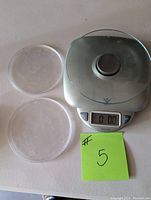 Front view of Taylor kitchen scale with two clear plastic covers beside it, displaying the digital screen showing 0.00
