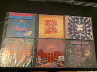 Front view of six sealed vintage music CDs arranged in two rows on a dark surface.