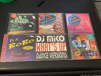 Front view of 7 vintage music CDs and CD maxi-singles arranged in two rows showing colorful covers and titles.