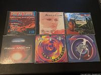 Front covers of six vintage music CDs in jewel cases, arranged in two rows on a dark surface.