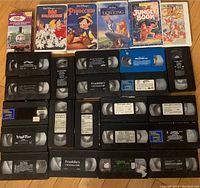 Top-down view of 26 VHS tapes including Disney movies and kids cartoons placed on a wooden floor.