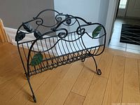 Side angle showing the foldable metal magazine holder with black wire frame and green leaf decorations.