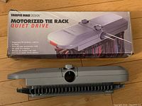 Motorized tie rack device next to its original box showing product image and description of the item.