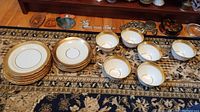 Six teacups and six saucers arranged on the floor with a carpet background.