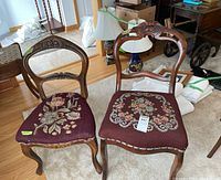 Two wooden framed chairs with floral needlepoint upholstered seats, showing the differences in backrest design and upholstery detail.
