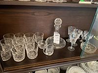 Photo showing full set of cut glass drinkware on shelf, including decanter, various glasses, sugar bowl, and creamer.