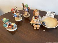 Overview photo showing four Goebel Hummel figurines and one ashtray on a wooden table.