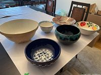 Six assorted mixing and serving bowls shown together on table including one large off-white Green's bowl and other patterned bowls.