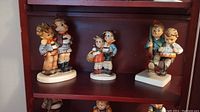 Three Goebel Hummel figurines displayed on a dark wood shelf, showing all three pieces in the set.