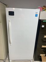 Front view of white upright freezer with a curved vertical handle and electronic control panel on upper door.