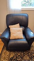 Front view of black leather recliner with two beige pillows on seat.