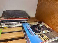 Wide view of stacked vinyl LP records on a bed frame showing album covers including Lightnin' Hopkins and orchestral titles.