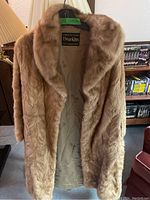 Full view of the light brown mink fur coat on a hanger revealing the length and drape, including attached scarf.
