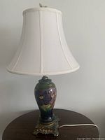 Full view of Moorcroft lamp on table showing white bell shade, pottery body and metal base