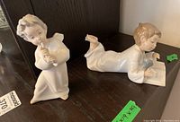 Both Lladro angel figurine and Nao child with puppy figurine together on shelf, showing overall size and condition