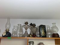 Shelf with multiple oil burning lamps and glass chimneys of various sizes and shapes.