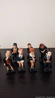 Seven Royal Doulton Dickens figurines with detailed painted features and Victorian-era clothing, arranged on a flat surface.