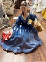 Full view of Royal Doulton HN 2429 porcelain figurine seated woman in blue dress holding a white hat with red bow.