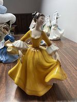 Side view of the Royal Doulton figurine showing the flow of the yellow dress and the white ruffled sleeve detail.