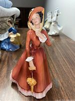 Front view of the Royal Doulton figurine showing the detailed painted face, orange dress with white trims, and yellow parasol.