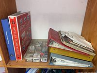 Photo of shelf with Harris Traveler Stamp Album, blue album, multiple plastic containers of loose stamps, and three binders containing loose stamps and papers.
