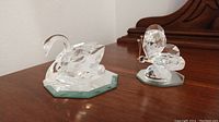 Two Swarovski crystal figurines on brown wooden surface. Includes swan and butterfly.